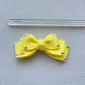 Macro detail of yellow ribbon bow accessory with rhinestones shown against a metric ruler - Yellow