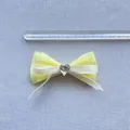 Dettaglio di un fiocco giallo a strati con gemma a cuore e righello di misurazione - Raso Giallo Con Nastri Sottili Crema (Stile 4)