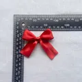 Detailed view of a 7.5cm red satin bow accessory showing exact size with a ruler - Red