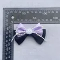 Detalle de un lazo artesanal lila y negro con rosa blanca y perlas sobre una regla - Púrpura