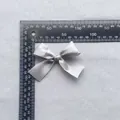 Macro detail of a 7.5cm grey satin ribbon bow accessory with ruler for size reference - Silver Gray (7)