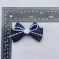 Detalle de lazo de seda azul con rosa de resina y perlas sobre tela gris fina - Azul marino