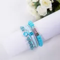 Detailed close-up of four-piece blue beaded bracelet set with alphabet and smile charms - Good Blue