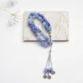 Tasbih islámico de ágata azul con borlas plateadas sobre una superficie de piedra clara - Azul