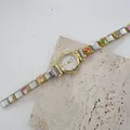 Dettaglio orologio quarzo donna con ciondoli smaltati colorati su cinturino oro e argento - Quadrante Bianco Ghiera Oro Fiori Smaltati