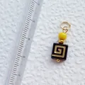 Detail view of a handmade geometric acrylic charm with gold patterns next to a ruler - Black Greek Fret Square Pendant (4)