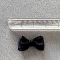 Mini black ribbon bow accessory showing 25mm size measurement on a gray woven background - Black