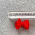 Close-up of a mini red ribbon bow next to a ruler showing its 21mm size for DIY crafts - Red