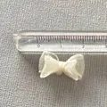 Detailed view of a 2cm mini organza ribbon bow measured with a ruler on grey fabric - Off White