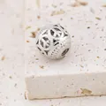 Vista macro di un ciondolo a sfera cava con simboli della pace incisi e motivi a onde - Stile Segno della Pace / Argento