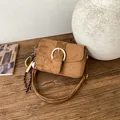 Retro brown suede shoulder bag with gold horseshoe buckle and baseball charm on a table - With Pendant / Brown