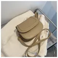 Detailansicht der beigen Satteltasche mit goldenen Beschlägen auf weißem Strickstoff - Khaki