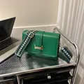 Detalle de bolso verde de piel con cierre dorado y correa ancha bordada con diseño moderno - Verde
