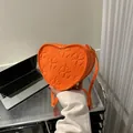 Detail of orange heart-shaped crossbody bag featuring embossed four-leaf clover patterns - Orange Red
