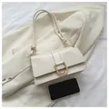 Close-up of cream shoulder bag with gold horseshoe buckle next to a smartphone - White