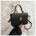 Nahaufnahme der schwarzen Retro-Handtasche mit goldener Schließe und Logo-Prägung - Schwarz