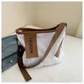 Detail der weißen Canvas-Tasche mit braunem Rand und FASHION-Lederanhänger im Bett - Weiß