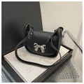 Detail of black mini crossbody bag featuring a silver bow metal buckle and leather strap - Black