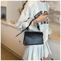 Close-up of black crocodile texture handbag with gold metal rings and knot handle - Black
