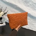 Orange quilted clutch bag featuring floral textured embroidery held by hand - Orange