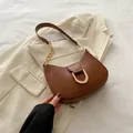 Minimalist brown leather dumpling bag with gold buckle and chain strap on a blazer - Brown