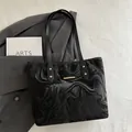 Bolso tote negro con textura fluida de mármol y detalles dorados sobre blazer gris - Negro