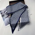 Detailed close-up of navy and white geometric silk twilly scarf on a wooden tray - Blue
