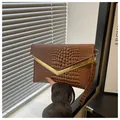 Detail of brown crocodile pattern envelope clutch with gold V-metal trim and wrist strap - Coffee