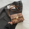 Chic leopard print crossbody bag with gold metallic clasp on grey suit background - Brown