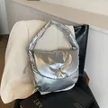 Metallic zilveren puffer schoudertas met een ronde flap en drukknoop op een leren stoel - Zilver