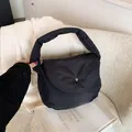 Minimalist black quilted puffer shoulder bag with metallic buckle on a stylish chair - Black