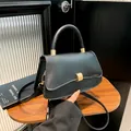 Bolso negro elegante con hebilla dorada en mesa de madera y fondo de cristal estriado - Negro