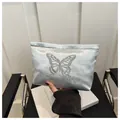 Detail view of butterfly embroidery on a satin cosmetic bag held by a person - Silver
