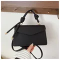 Detail view of black woven texture handbag with knot handle and metal-tipped decorative cords - Black
