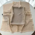 Elegant beige silk square scarf with black polka dots draped on a minimal white table - Khaki