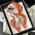 Detailed view of luxury silk scarf with orange equestrian chain and tassel patterns - Orange