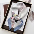 Nahaufnahme von Seiden-Halstuch mit Paisley-Blumenmuster in einer eleganten Geschenkbox - Azurblau