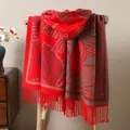 Detail of red leaf pattern shawl with fringe on wooden stool in warm home setting - Red