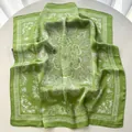 Detailed view of light green silk scarf with white floral patterns on a table - Green
