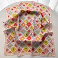 Detailed close-up of a pink square silk scarf with summer stamp patterns on a white table - Off White
