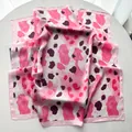 Close-up of pink leopard print silk scarf with smooth satin finish on white surface - Pink