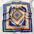 Square silk scarf with blue and orange geometric diamond patterns on white desk - Blue