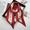 Close-up of red twilly silk scarf featuring horse carriage print and 100% polyester label - Red