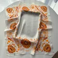 Detailed view of square silk scarf with orange floral print draped on a table - Sunflower Yellow