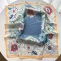 Close-up of elegant floral silk scarf with vibrant blue patterns and orange piping detail - Yellow