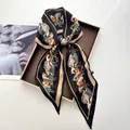 Detail of silk twilly scarf with elegant horse print tied in a bow on a display tray - Black