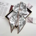 Close-up of a bow-tied silk scarf featuring botanical leaf prints and dark brown borders - Khaki