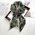 Detailed view of dark green silk scarf with white leaf print tied in a knot on a magazine - Green