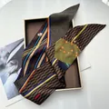 Macro detail of high-quality striped silk scarf featuring geometric patterns and sheep logo - Coffee