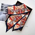 Detail of horse-print twilly silk scarf in orange and navy blue inside a gold gift box - Orange Red